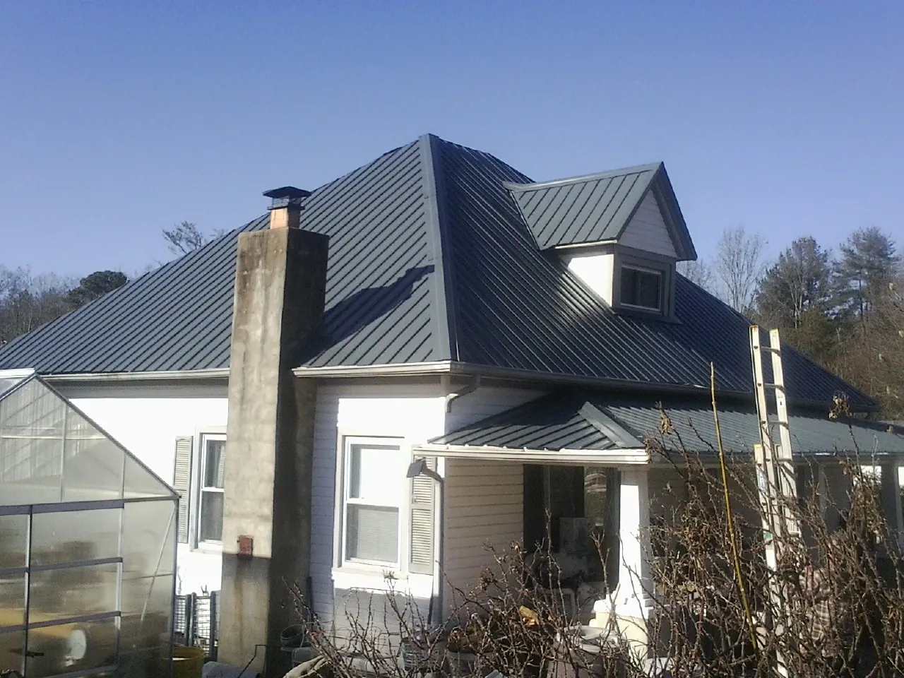 Dark blue standing seam metal roof on a white farmhouse with dormer — Slate & Tile Roof Repair by Roofing Brothers in Harrah