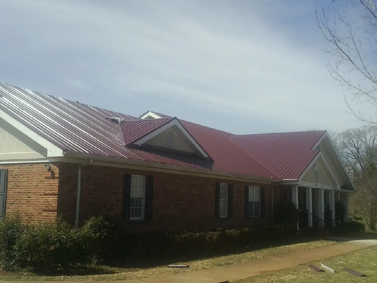 Red metal roof with gabled entries on a long brick building, from a Hail Damage Roof Repair job in Harrah