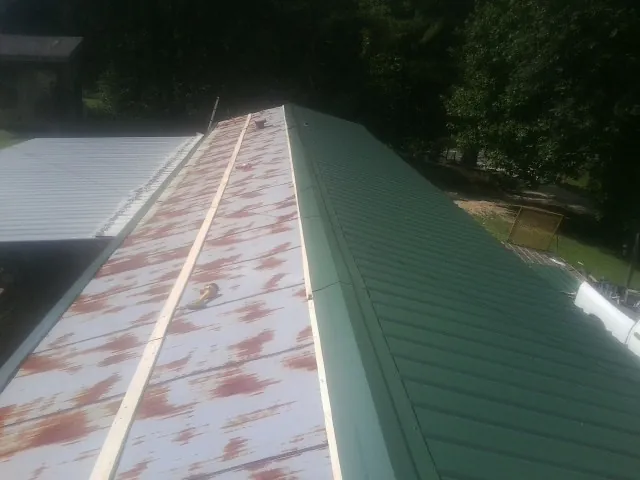 Old rusted panels beside newly installed green metal roofing — Wind Damage Roof Repair by Roofing Brothers in Harrah