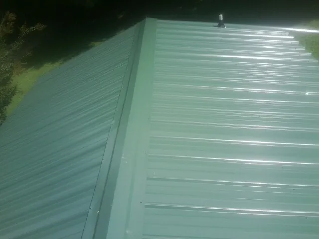 New green metal panels meeting at the ridge of a roof — Flat Roof Repair work by our crew in Harrah