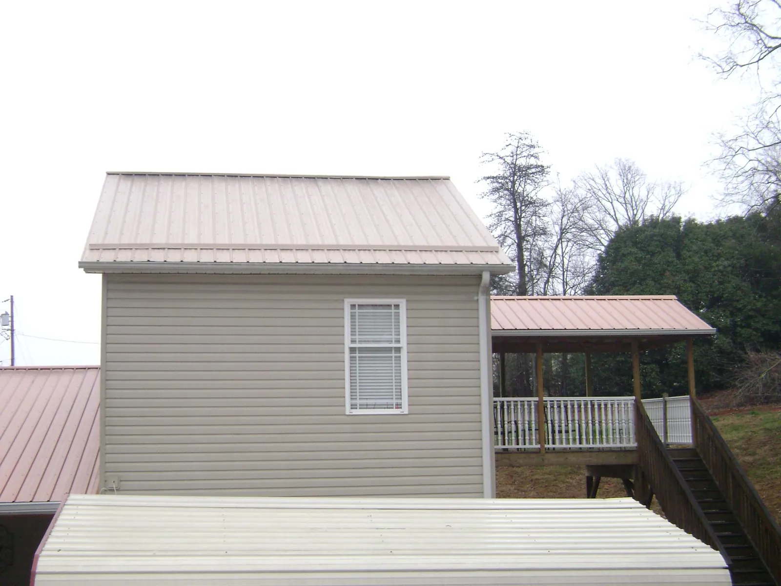 Tan metal roofs on a two story addition and attached porch, from a Roof Replacement job in Harrah
